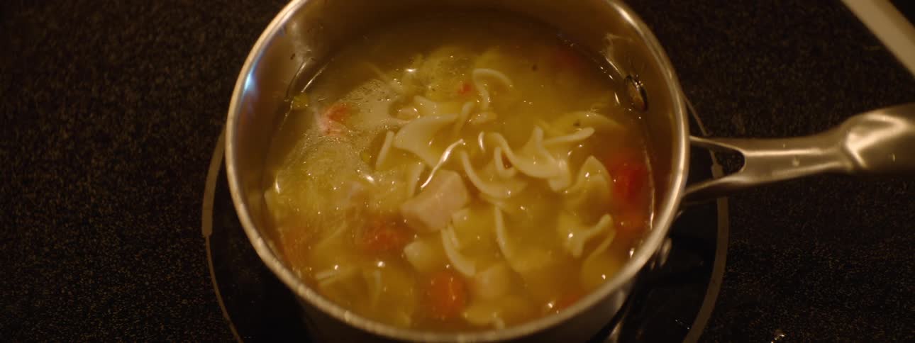 The contents of a can of noodle soup is poured into a metal pot on a stove top