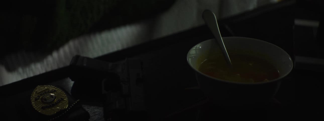 A close up shot of a bowl of soup a police badge and a handgun over a table in an indoor setting