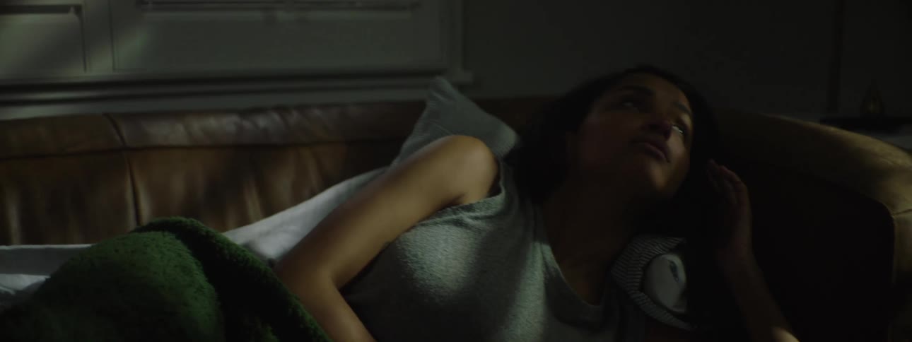 In the video a woman is seen lying on a bed with a green blanket draped over her she looks distressed with tears in her eyes and is breathing heavily