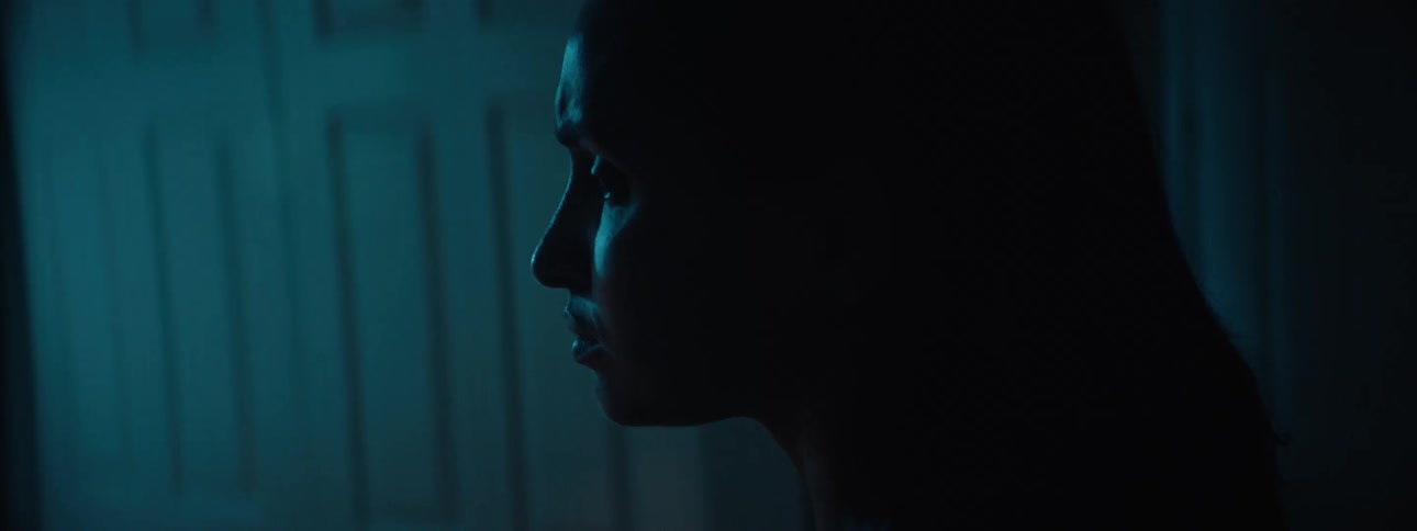 Young woman enters a dark room looking sad as faint sunrise light reflects through the window