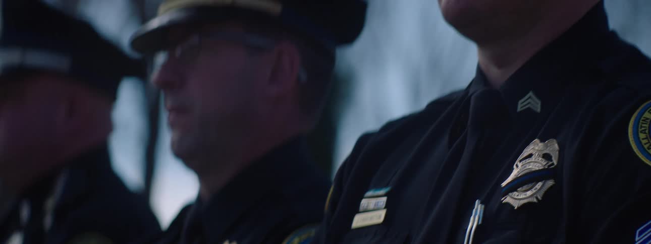 Three law enforcement officers in uniform standing still in a cemetery during a funeral service