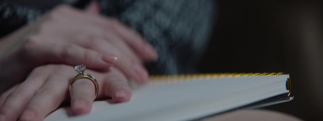 A woman wearing a diamond ring rests her hands on a notebook