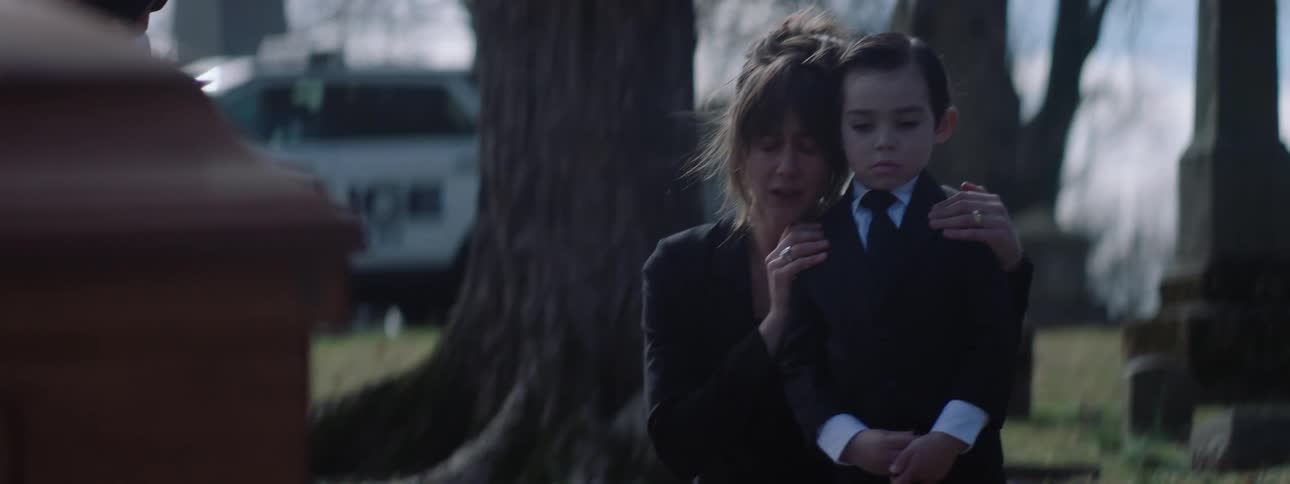 A woman kneels down to console a boy standing at a tombstone