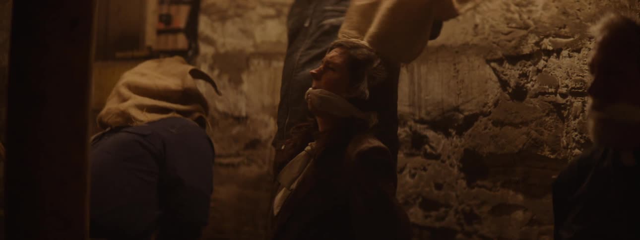 A captivity setting with three hostages and a man taking off a sack of their heads