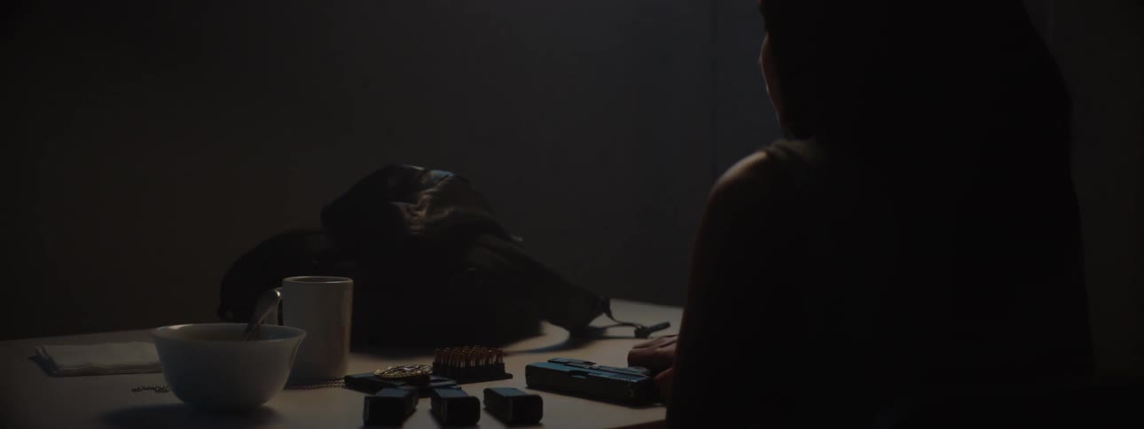 A persons hands load bullets into a gun magazine on a dimly lit table next to a pistol