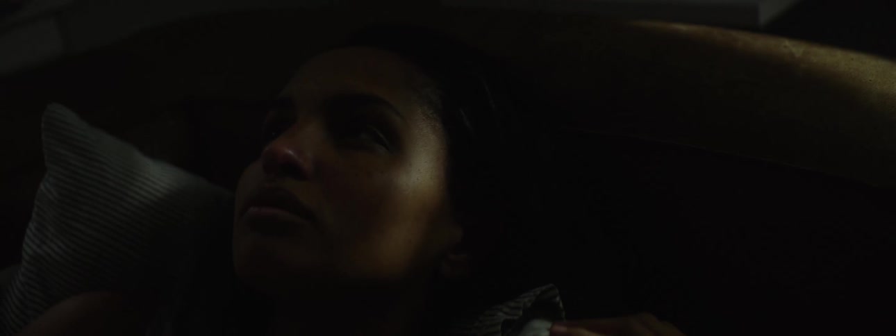 In the video a woman is seen lying down in a dark room with only her face and shoulder visible in the low light she appears to be listening intently to something and a faint reflection can be seen in her eye