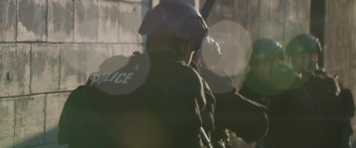 A group of trained police officers tactically approach a building entrance during daytime