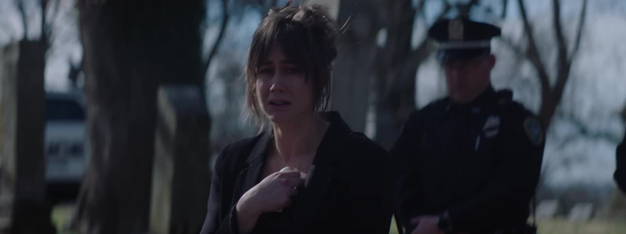 A woman mourns at a funeral while a police officer stands nearby