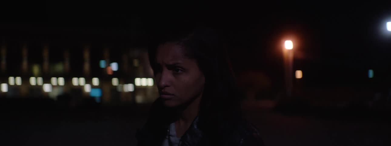 A person walks on a street in the dark turns a head to the side and walks toward the camera