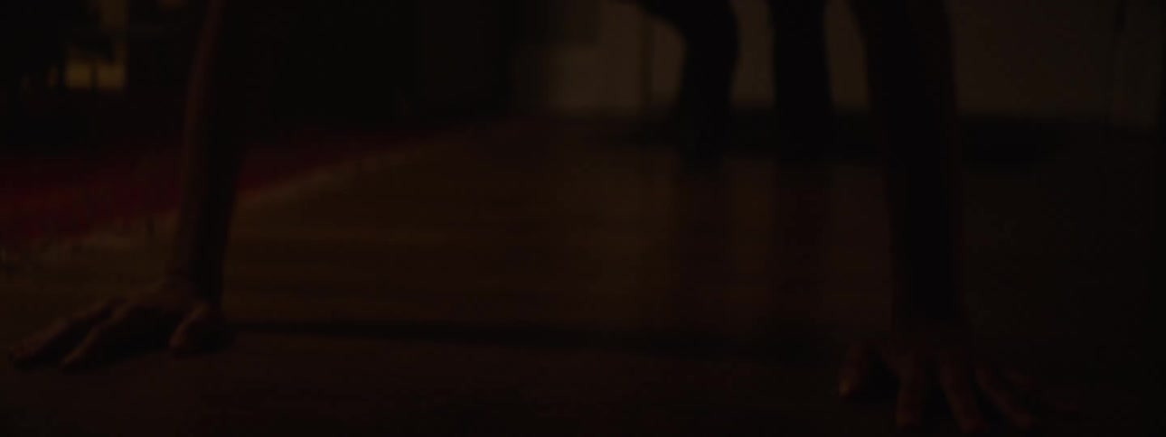 Woman with tired expression tying her hair while standing in a dark room of the house