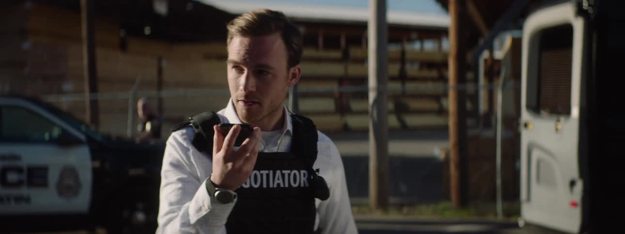 Man wearing a vest labeled negotiator speaking on a radio during a police operation