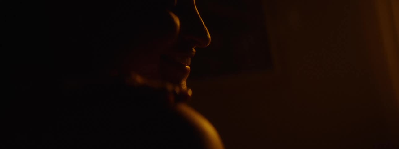 A woman smiles gently in warm orange light with a hand on her shoulder