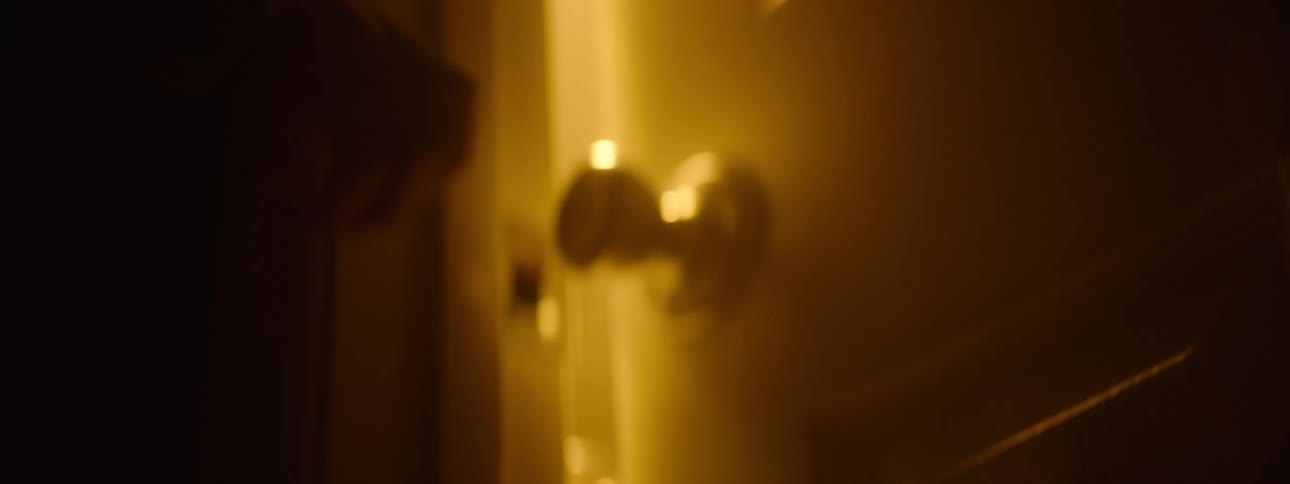 A hand reaches for a doorknob in warm orange light
