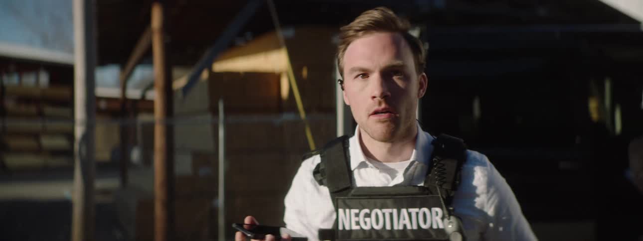 A police officer talking on a cellphone and with a worried expression on an outdoor setting with a police car in the background