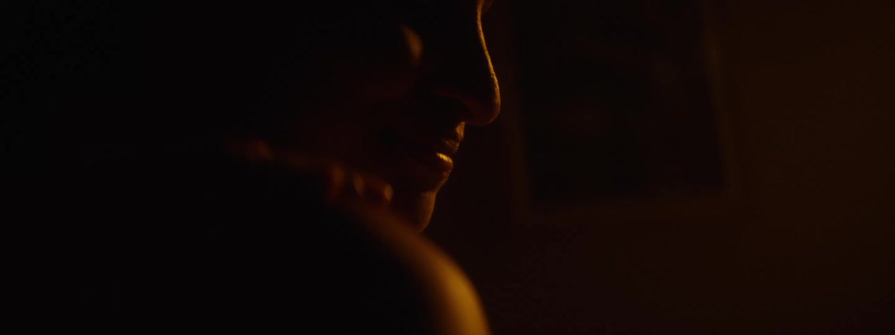Someone puts their hand on a womans shoulder and she smiles in a dimly lit room