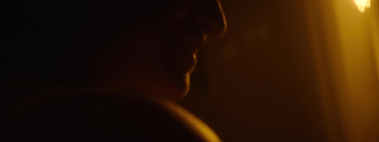 A dimly lit side profile of a smiling person their face softly illuminated by warm orange light