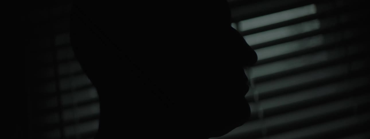 Man in a dark room at night with a window faintly reflecting light from outside