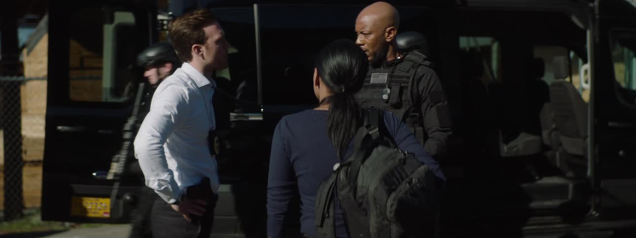 Male and female law enforcement officers walking toward another officer and engaging in a discussion at a city crime scene
