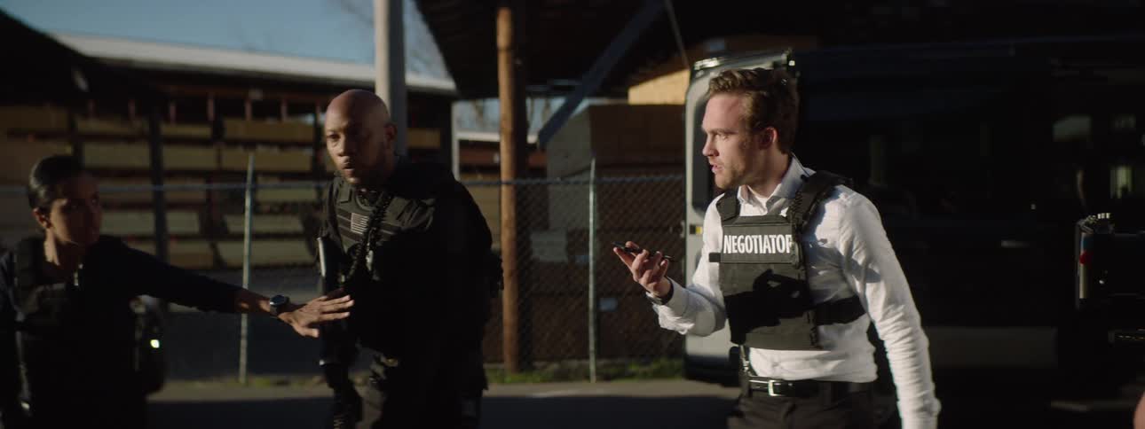 A negotiator working with other law enforcement agents making a phone call while standing outdoors during daytime