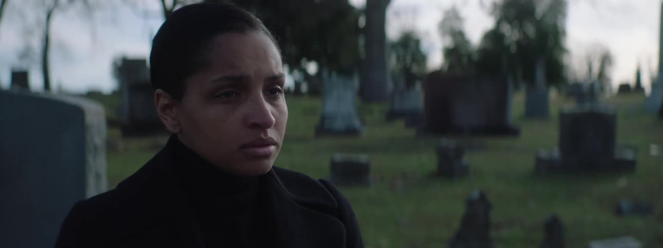 A persons face in a cemetery and then the person turns and walks away from the camera