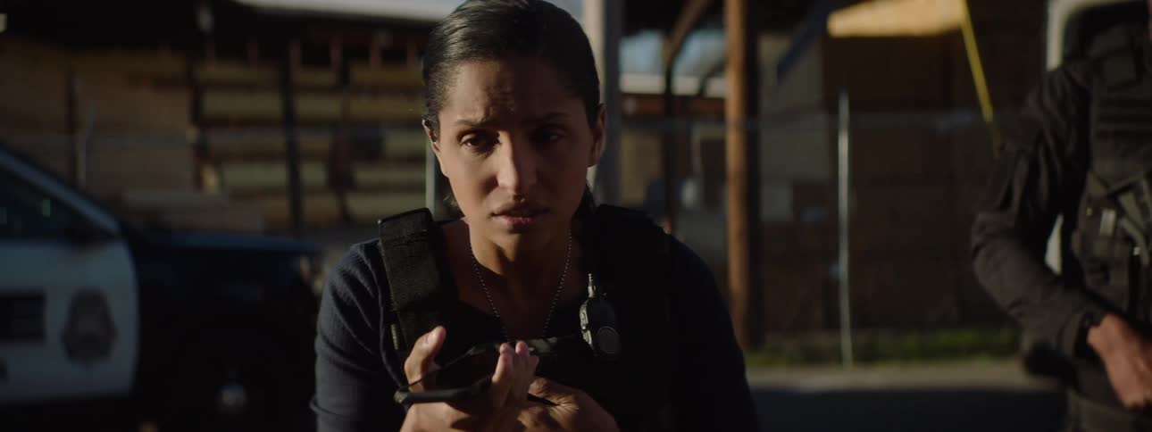 During a tense standoff a female detective urgently speaks into her radio while a negotiator and a swat officer stand by