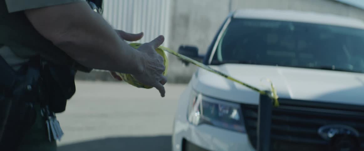 Police officer stretching yellow caution tape in front of patrol cars