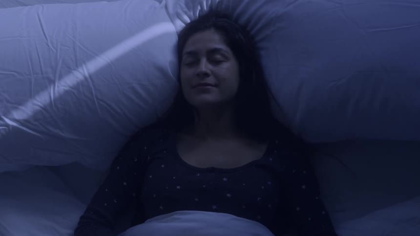 A close view shows a woman with long dark hair lying on a bed with her eyes closed