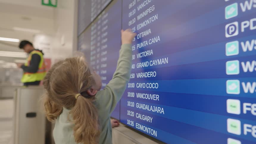 A child looks at a departure board and points at the information with a hand