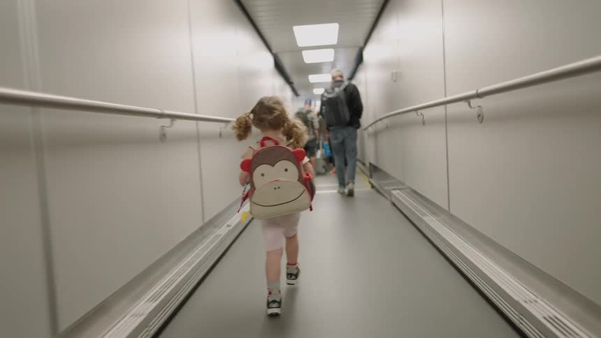 Child carrying a backpack walking along a jet bridge meeting several adults in the terminal as passengers onboard or offboard a flight