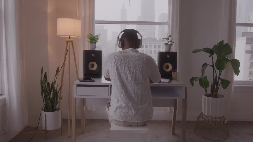 A man sits at a desk with two speakers on it while he puts headphones on