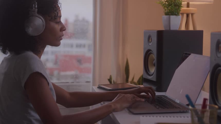 A woman wearing headphones works on a laptop at a desk
