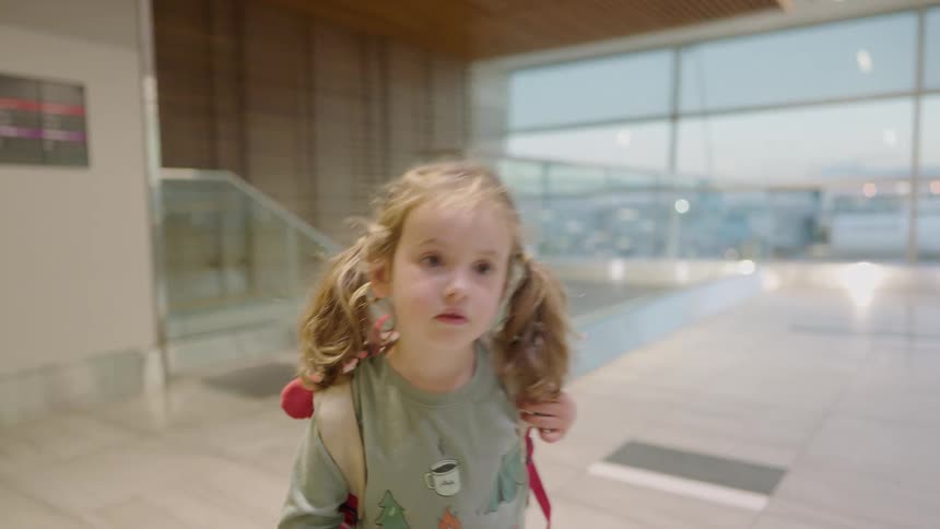 A video shows a young girl walking with a backpack on their back in an indoor setting