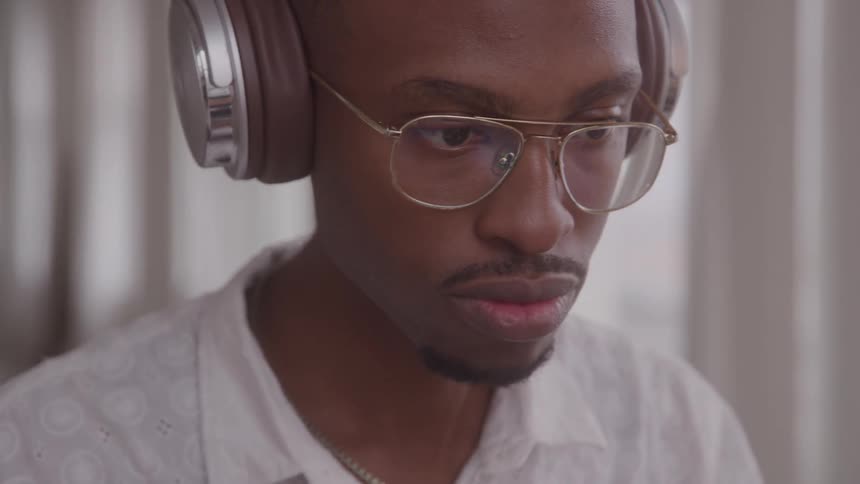 Close up portrait of a young black man wearing headphones while sitting in a room during daytime