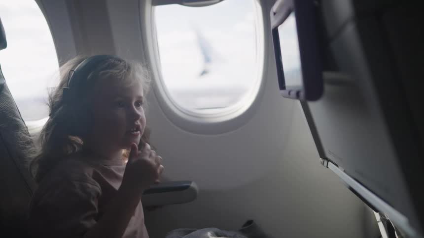 Child wearing headphones sitting in an airplane seat looking at the screen