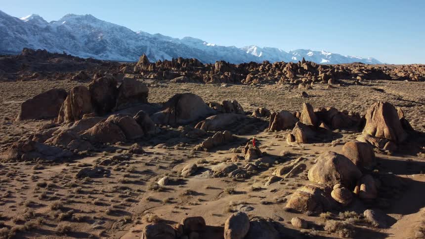 A rocky and hilly landscape is surrounded by towering snow covered mountains