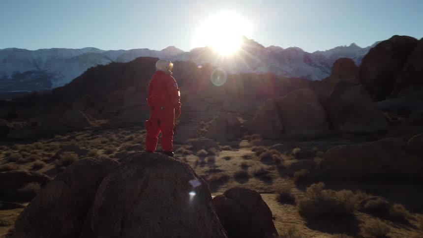 An orange suited astronaut standing on a rock in a desert during daytime