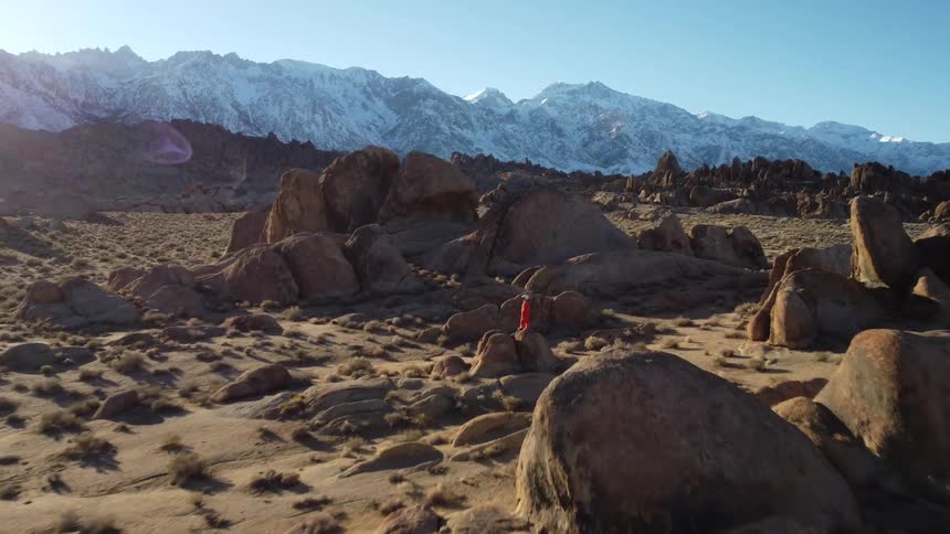 Person in an orange exploration suit among desert rocks with mountains in the background