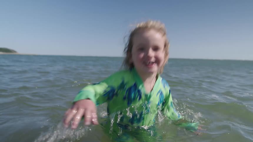 Young female child running in the shallow water at the beach submerged up to her waist joyfully playing under the midday sun