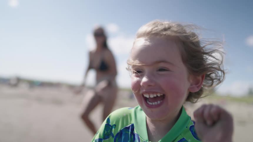 Smiling girl running on the beach alongside her mother in a bikini