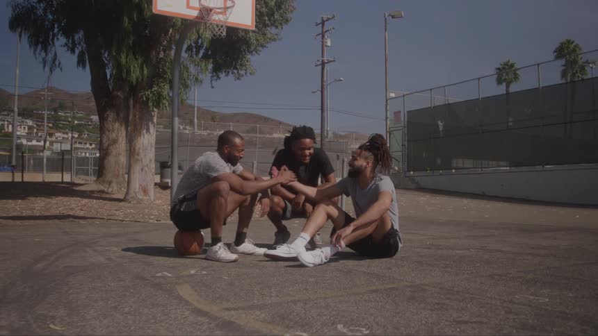 Three young people are sitting on a basketball court with two of them with their hands together over a basketball and the third person is looking at them