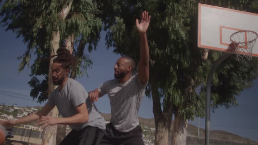 Three men play basketball on an outdoor court
