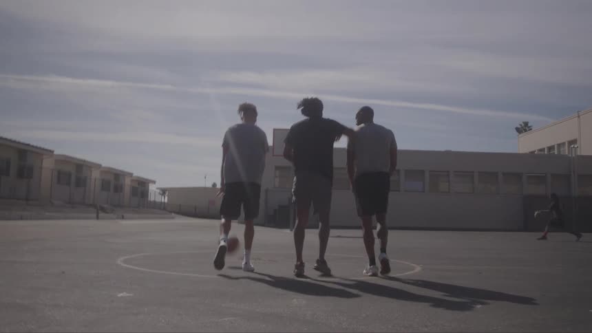 Three young men walking together on an empty basketball court seen from behind