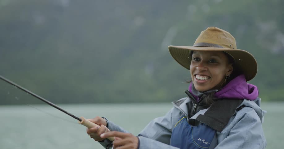 Woman smiles while holding a fishing rod at a lake