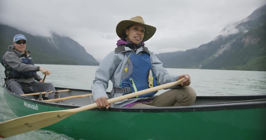 Man and woman rowing a boat on a lake at midday both wearing hats