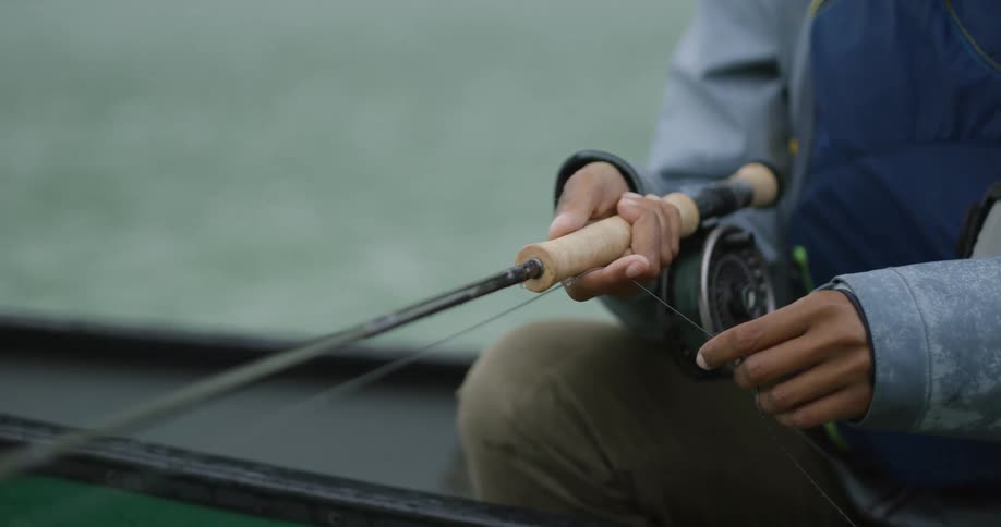 Man sitting in a canoe on a river at midday holding a fishing line as he fishes peacefully