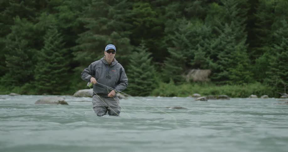 Man fishing in a shallow river surrounded by trees