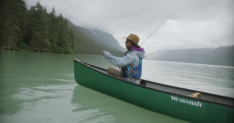 Woman fishes while sitting in a green canoe on the lake