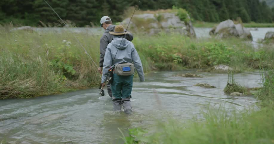 Two fishermen walking through the stream with rods and gear