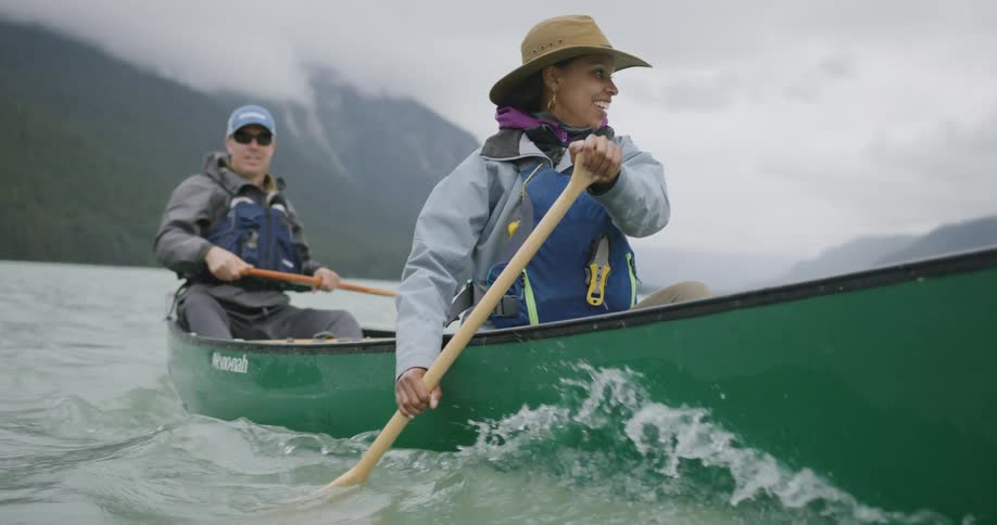 Couple paddling a green canoe on a lake surrounded by mountains