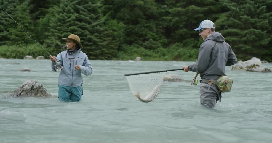 Woman smiling while man holds a net with a fish in the river